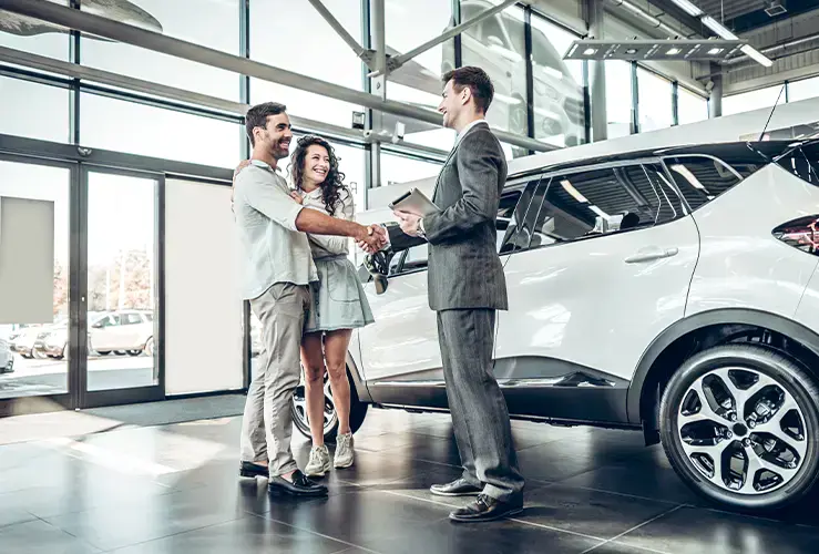 A salesman shaking hands with a couple in a car showroom