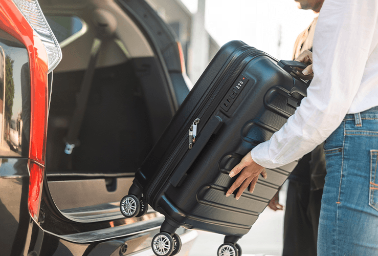 A person putting a suitcase in the boot of a car