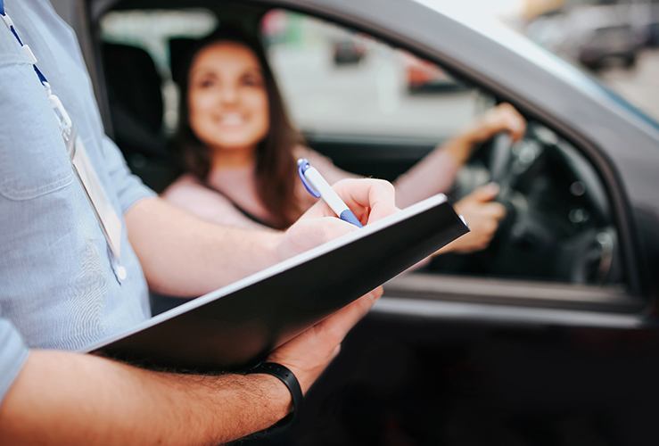Instructor writing on a clipboard with learner driver in background