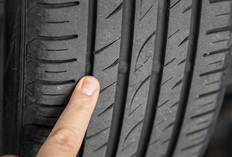A person using their finger to check the tyre tread depth