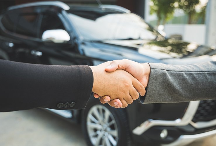 People shaking hands in front of a car